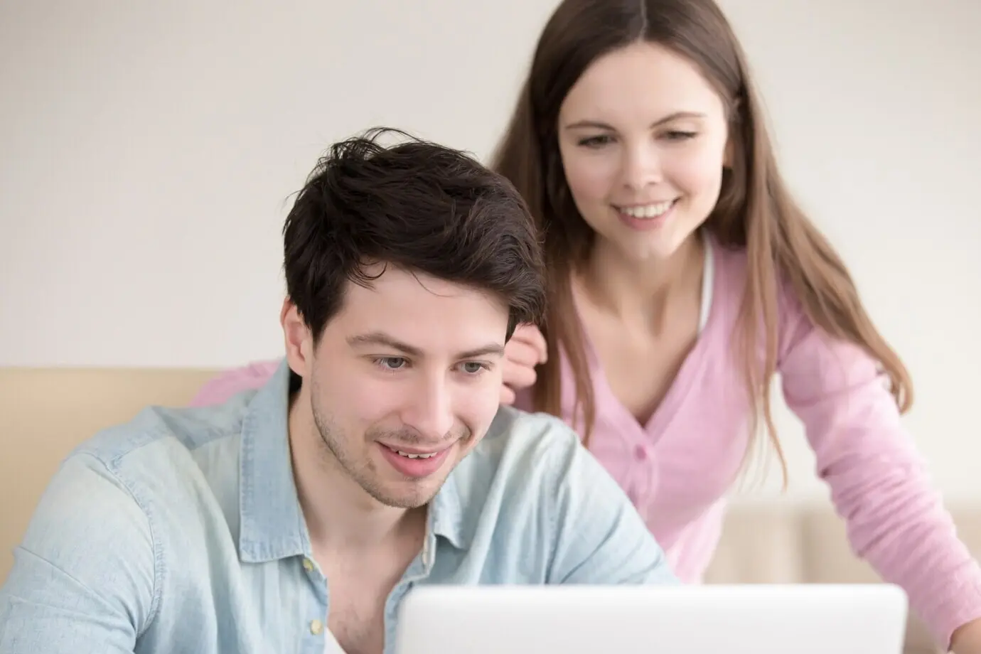A smiling young man and woman using a laptop computer indoors.